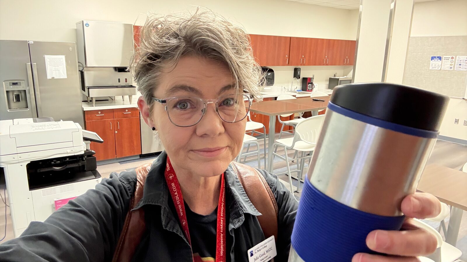 Julie Good holding a coffee mug in the Good Creative Media office, lanyard on
