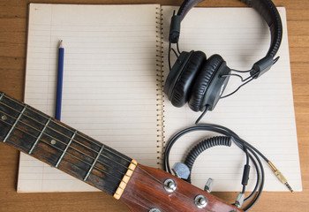 A notebook, headphones and an acoustic guitar on a desk